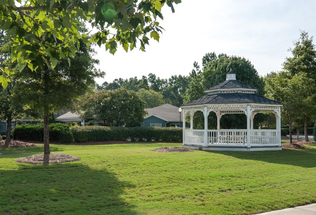 A serene park featuring a gazebo surrounded by a lush, green lawn and trees.