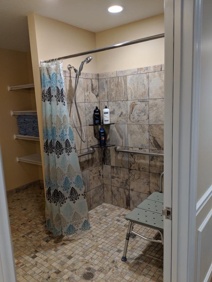 An accessible shower with a bench, tiled walls, and a patterned curtain.