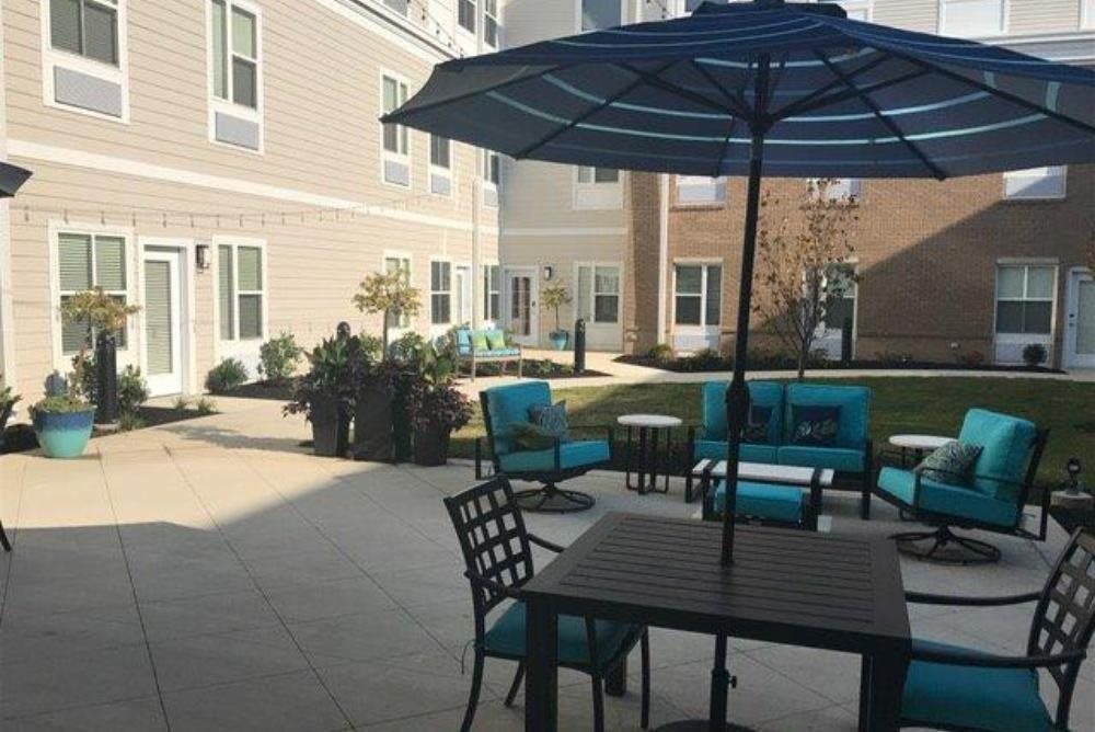 A courtyard with patio furniture and a large umbrella, surrounded by a building.