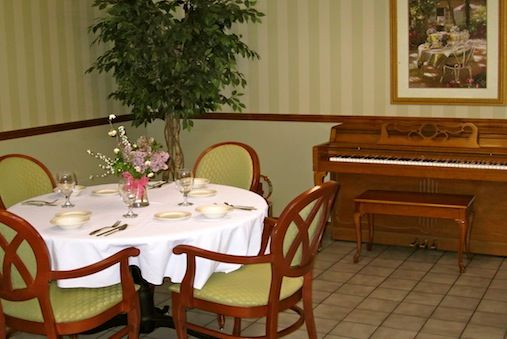 A dining area featuring a round table with chairs, set with floral decorations and a piano in the background.