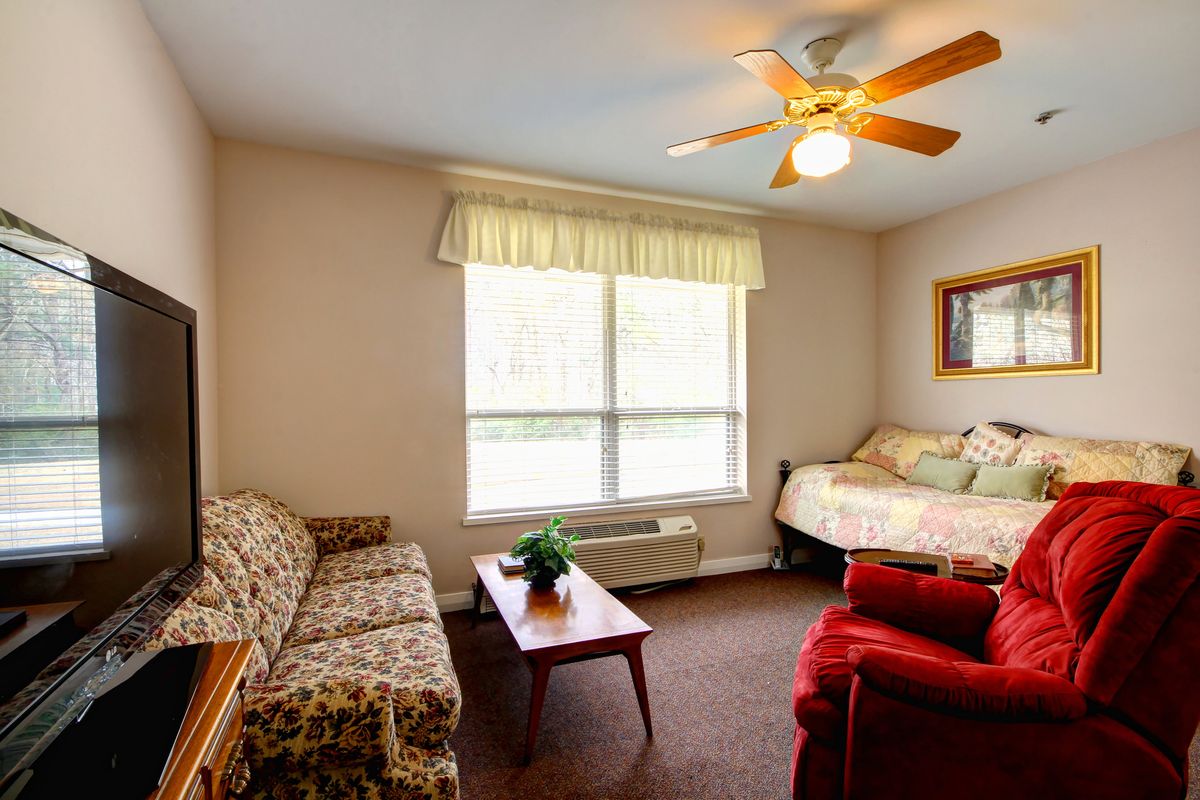 A cozy living space featuring a sofa, bed, and a ceiling fan near a large window.