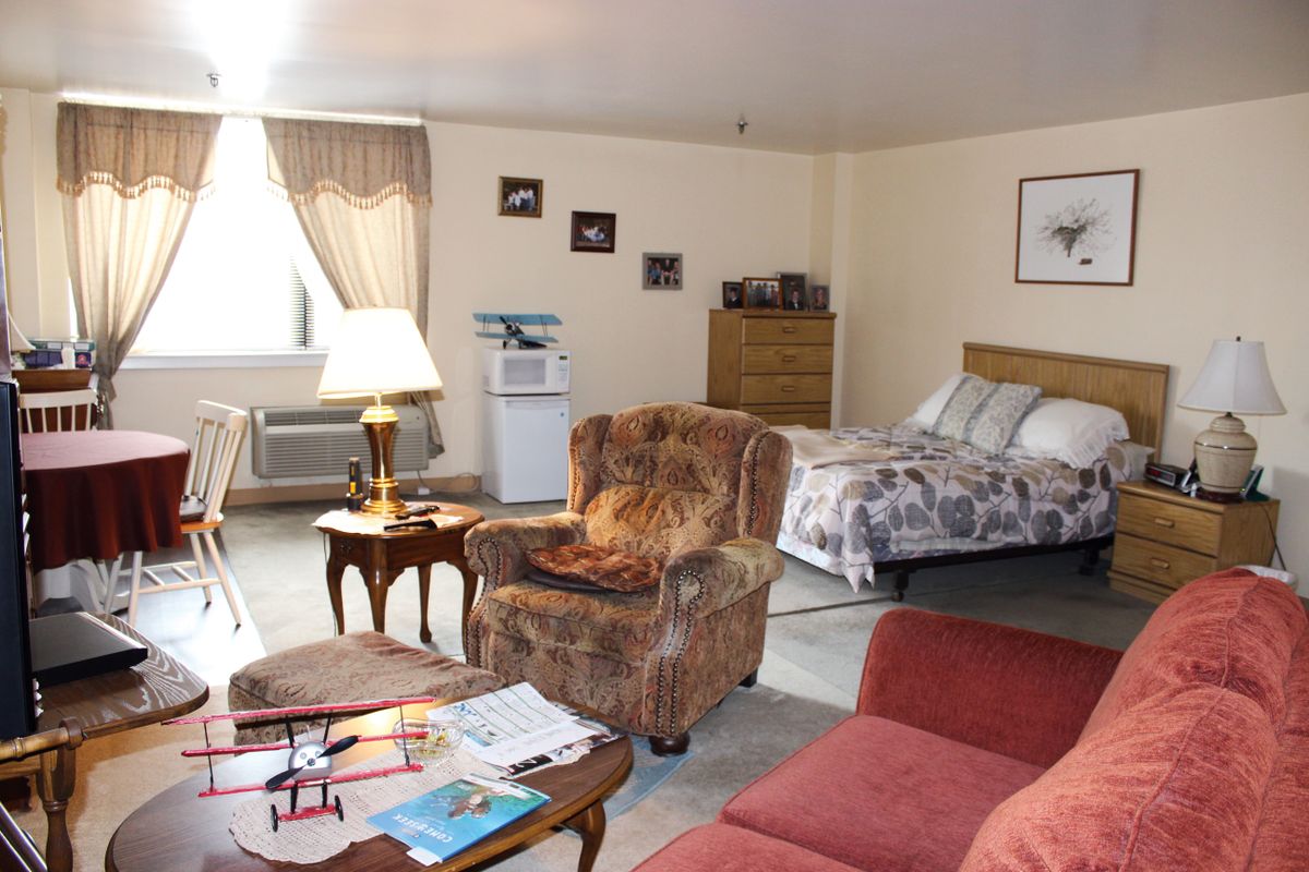 A cozy living space featuring a bed, armchair, sofa, and wooden side tables with a lamp.