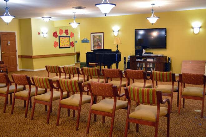 A well-arranged conference room featuring rows of chairs facing a piano and a television, with artwork on the walls.
