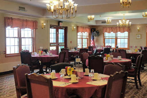 A cozy dining room set up for a meal, featuring red tablecloths and decorative chandeliers.