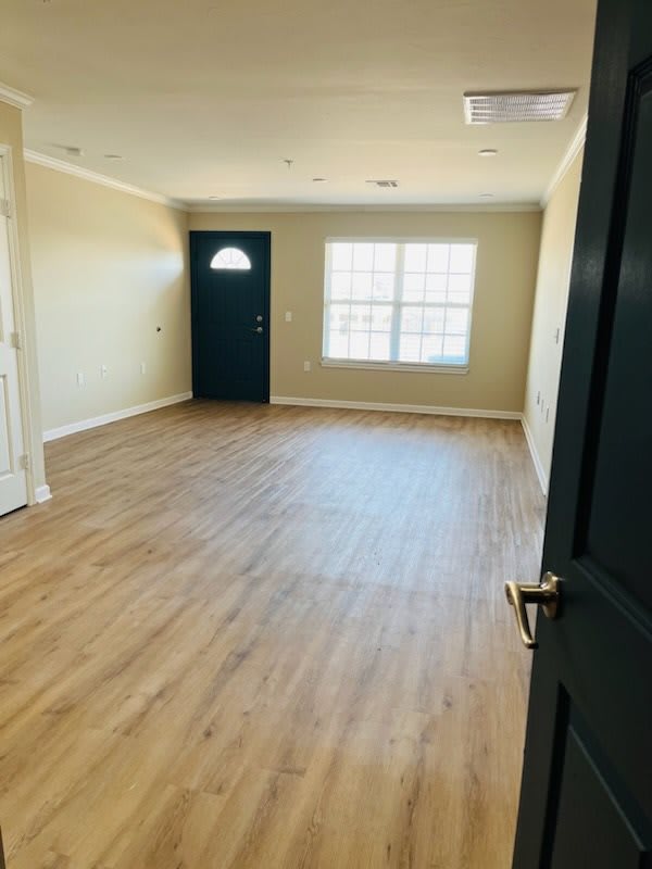 An empty room with wood flooring, a window, and a door letting in natural light.