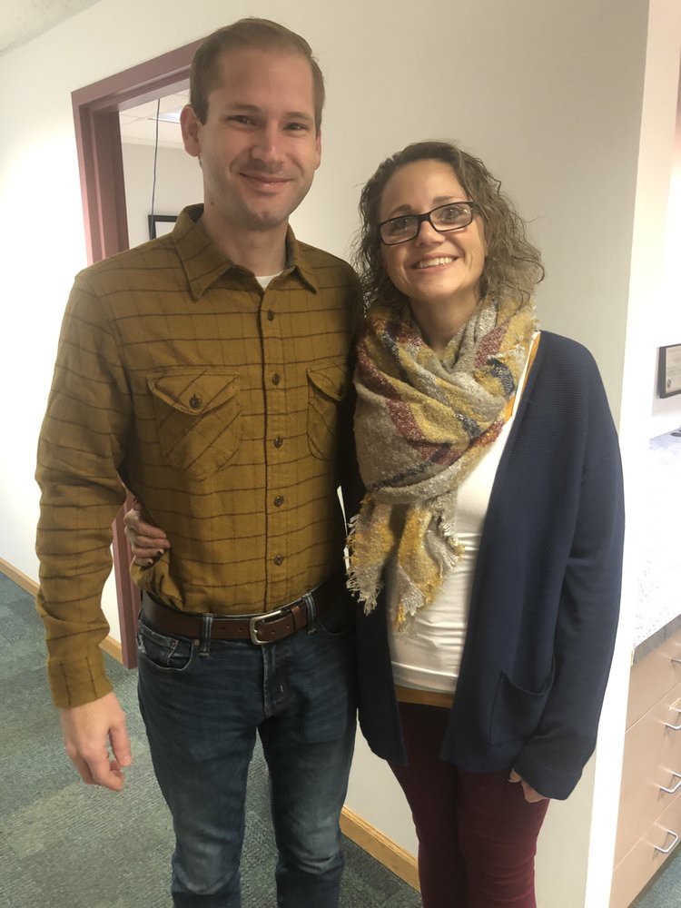 A smiling couple posing together indoors, wearing casual clothing.