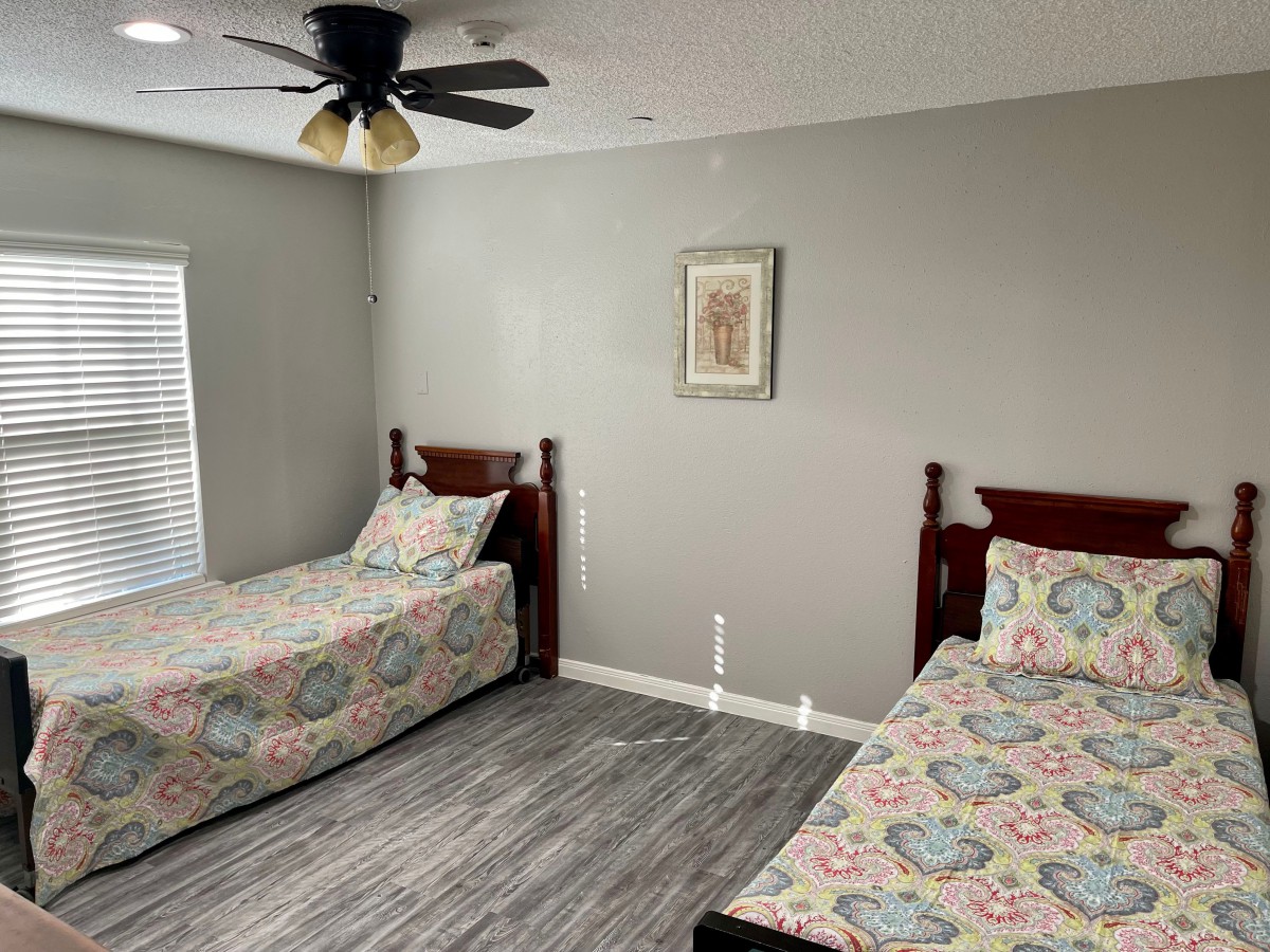 A cozy bedroom with two single beds, a ceiling fan, and simple decor.