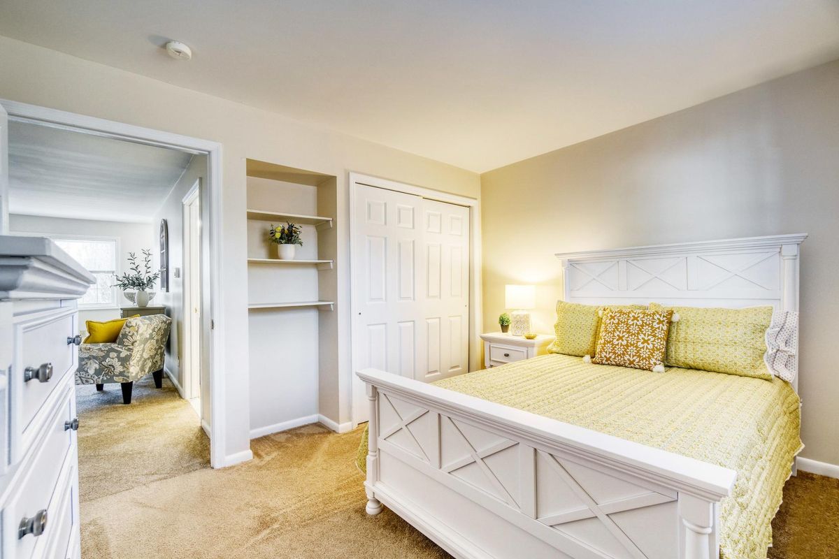 A cozy and well-lit bedroom with a white bed, decorative pillows, built-in shelves, and a bedside lamp.