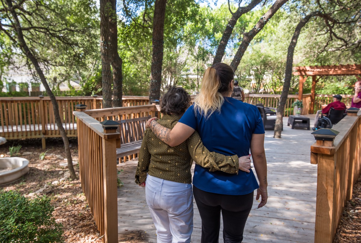 Two people walking arm in arm on a wooden path surrounded by trees.