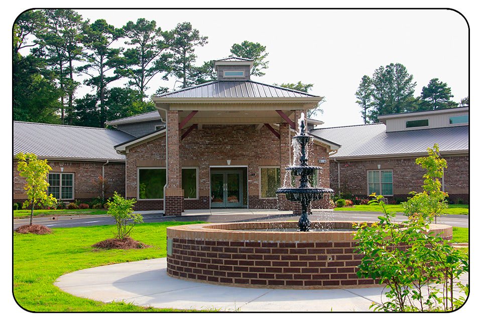 A brick building with a central entrance and a fountain in the foreground surrounded by well-maintained landscaping.