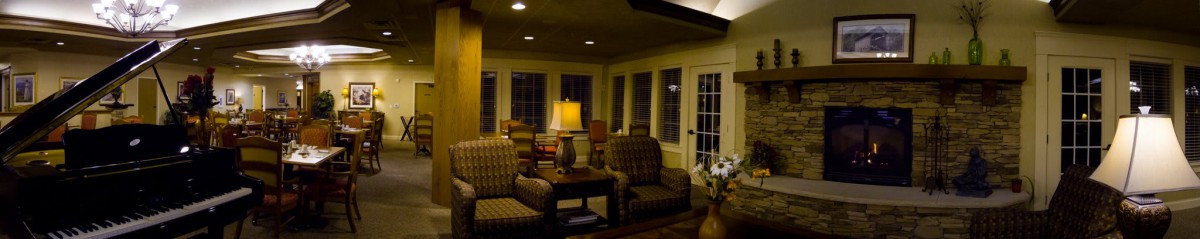 A cozy living room featuring patterned chairs, a table with a lamp, and large windows.