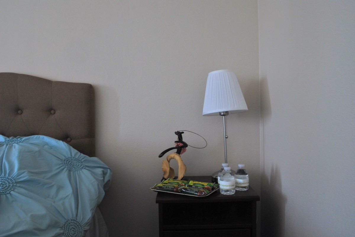 A tidy nightstand with a lamp, book, and water glass beside a bed.