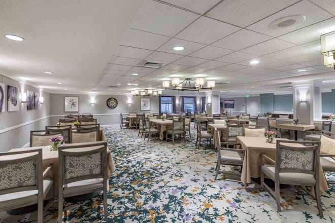 A spacious dining area with neatly arranged tables and chairs, elegant chandeliers, and a patterned carpet.
