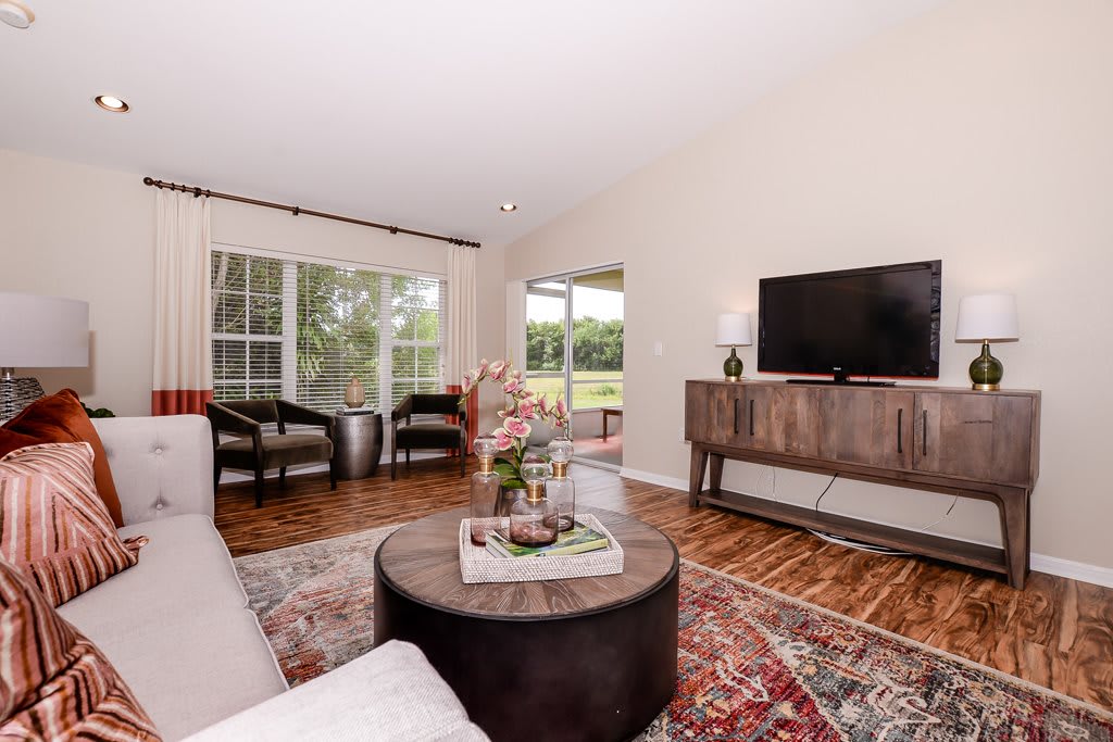 A cozy living room featuring a sofa, coffee table, TV, and large windows letting in natural light.
