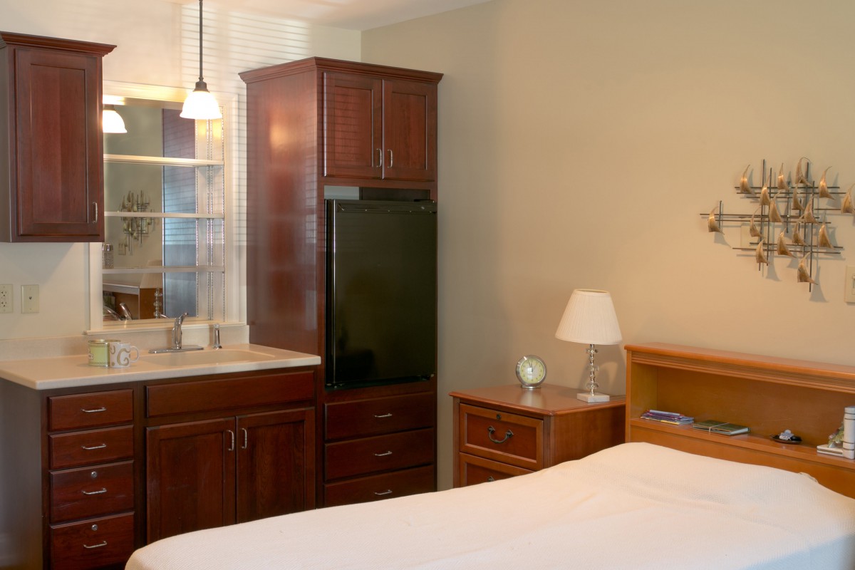A cozy bedroom with wooden furniture including a cabinet and nightstand, featuring a comfortable bed and a lamp.
