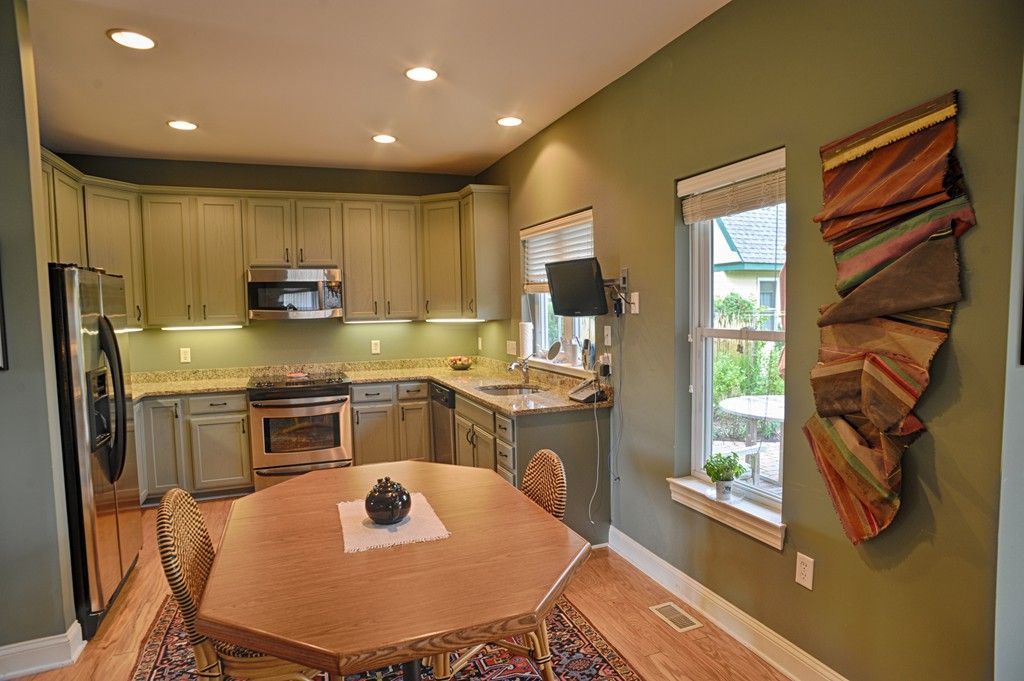 A modern kitchen with green walls, featuring a wooden dining table and contemporary appliances.