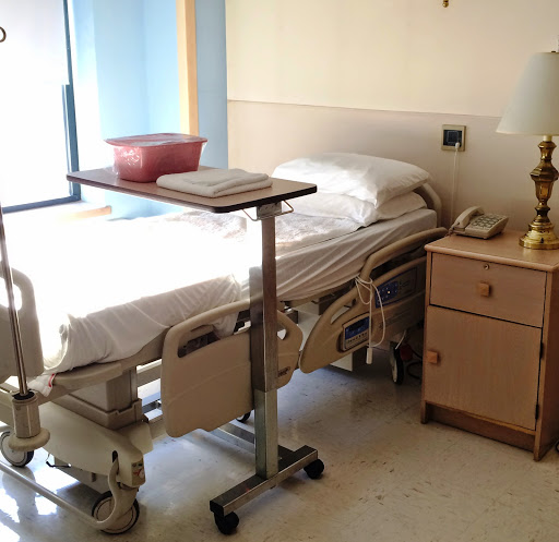 A hospital patient room featuring a bed, bedside table, and medical equipment.
