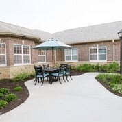 A cozy outdoor patio area with a table, chairs, and an umbrella surrounded by a landscaped garden.