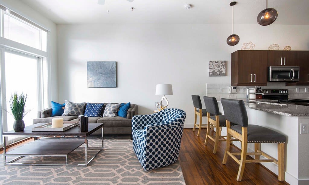 A modern living room featuring a stylish sofa, a patterned armchair, and bar stools at the kitchen counter.