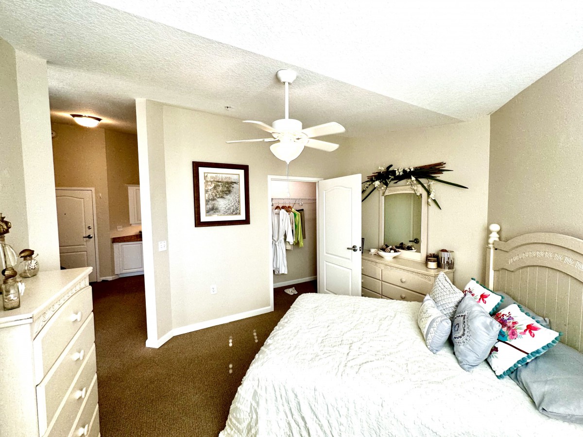 A cozy bedroom featuring a neatly made bed, ceiling fan, dresser with a mirror, and wall decorations.