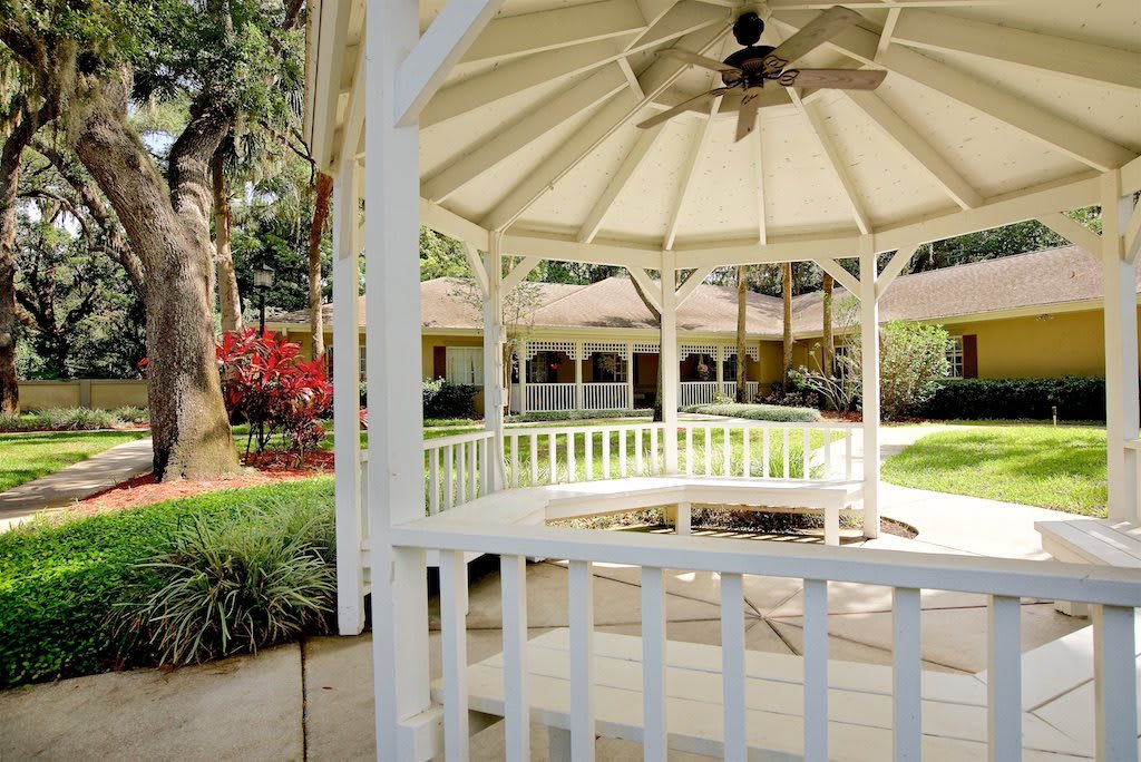 A white gazebo surrounded by a lush garden and colorful flowers.