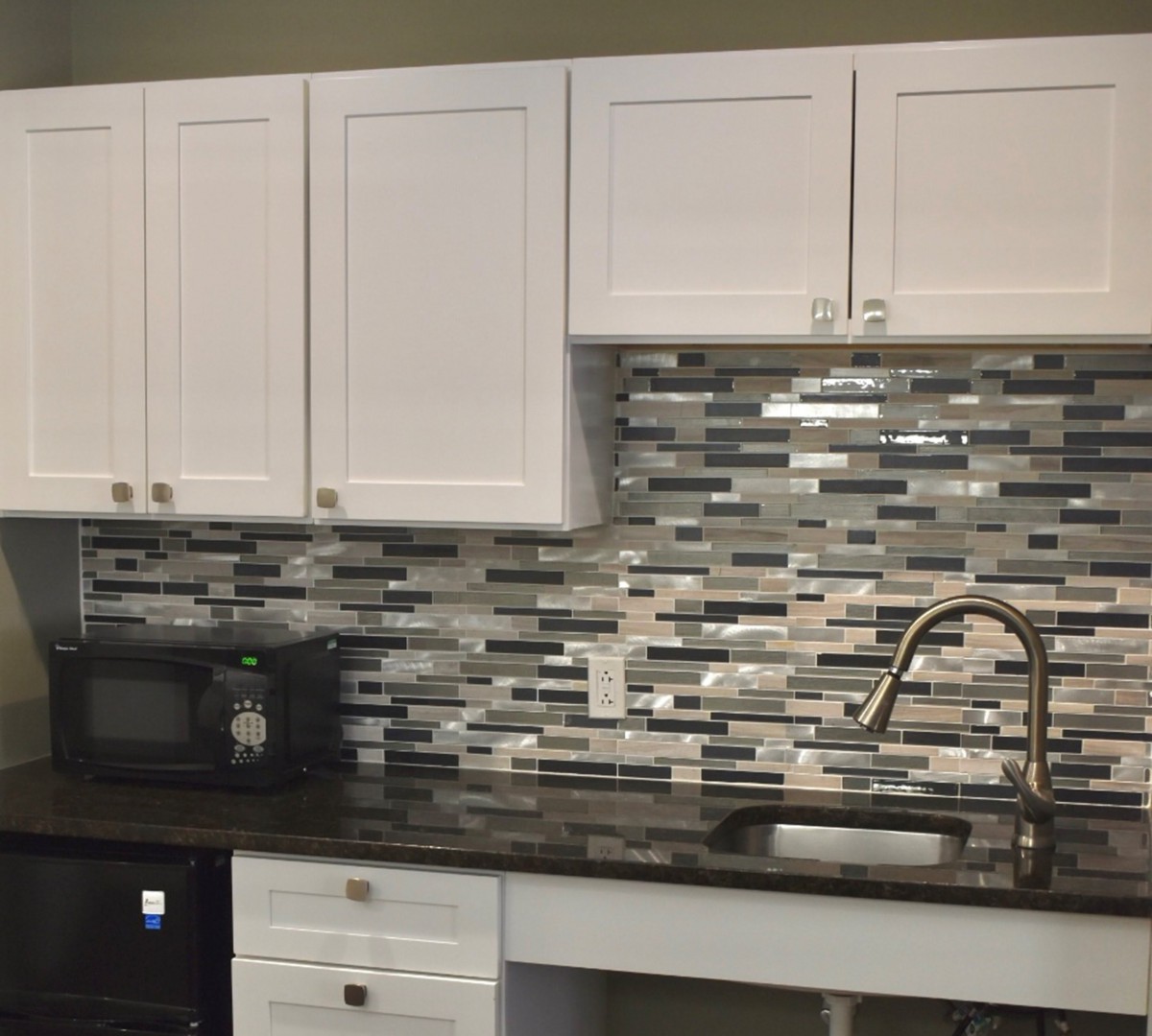 A modern kitchen setup featuring white cabinets, a tile backsplash, and a sleek countertop with a sink and faucet.