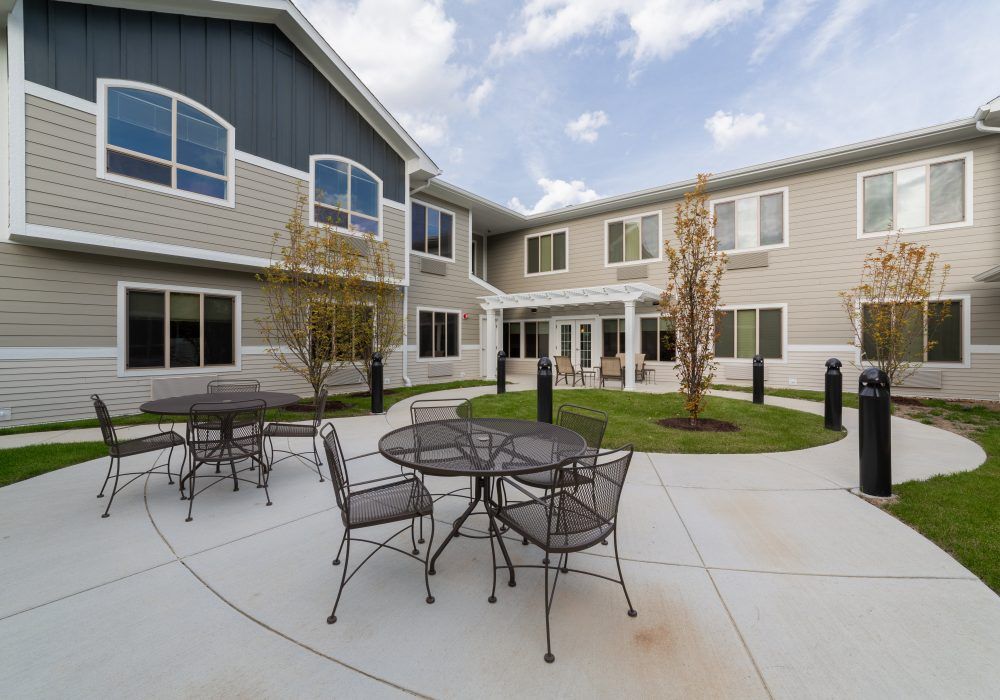An outdoor courtyard with metal tables and chairs surrounded by a two-story building.
