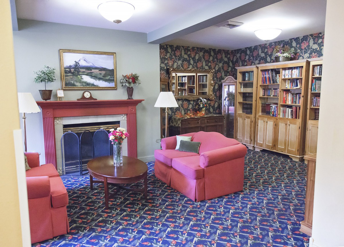 A cozy living room with red armchairs, a fireplace, and bookshelves filled with books.
