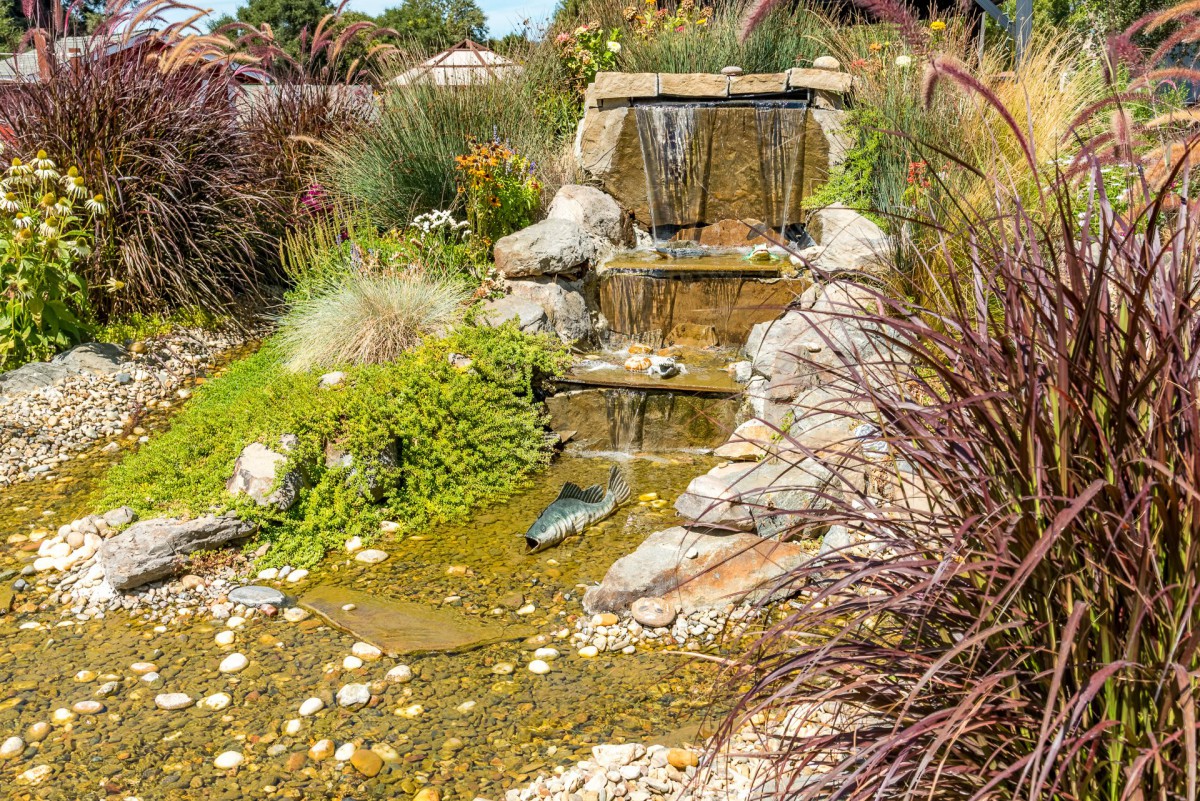 A serene garden with a small cascading waterfall surrounded by lush plants and rocks.