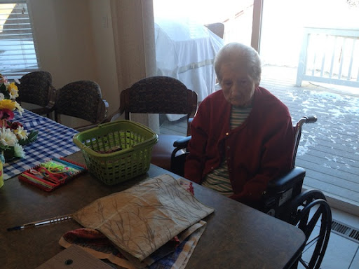 An elderly person sitting at a table with a basket in a cozy indoor setting.