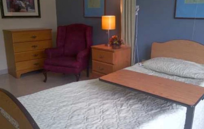 A cozy bedroom with a bed, nightstand, lamp, and an upholstered chair.