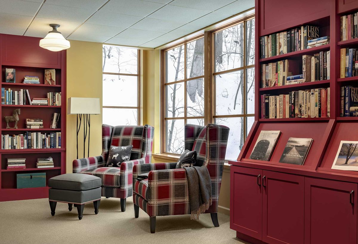 A cozy reading nook with plaid chairs and bookshelves by a large window overlooking a snowy landscape.