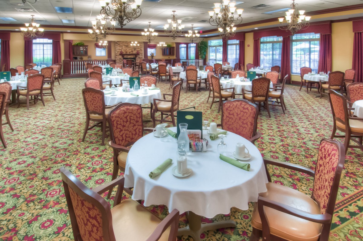 An elegant dining room with neatly arranged tables and chairs, featuring decorative lighting and a carpeted floor.
