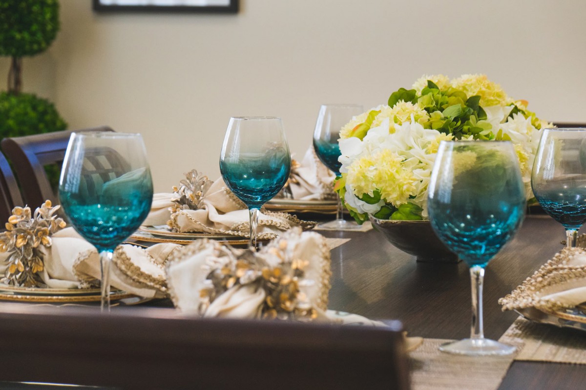 An elegantly set dining table with blue wine glasses and a floral centerpiece.