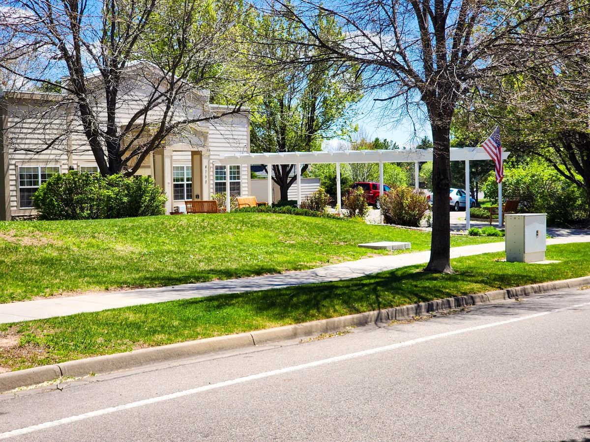 A suburban house with a well-maintained lawn and trees under a clear blue sky.