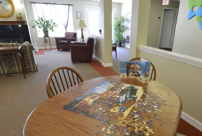 A cozy living room with a jigsaw puzzle in progress on a round table, surrounded by wooden chairs.