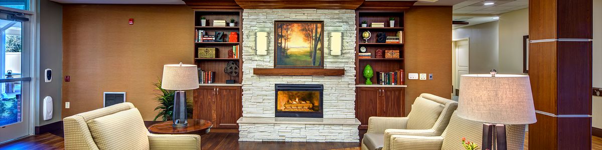 A cozy living room features a stone fireplace with an artwork above it, flanked by built-in wood shelves and soft lighting.