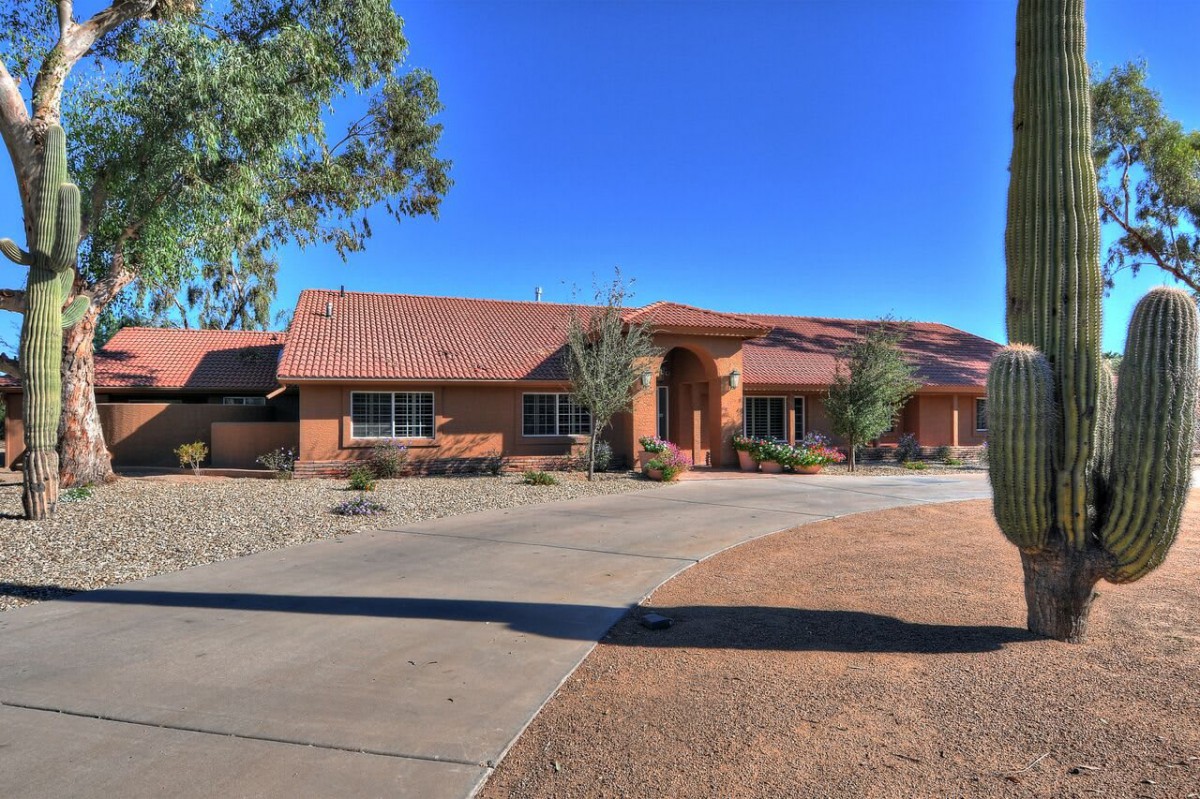 A single-story house with a wide driveway in a desert setting under a clear blue sky.