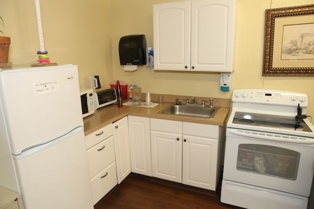 A compact kitchen with white cabinets, a stove, refrigerator, and small appliances on the countertop.