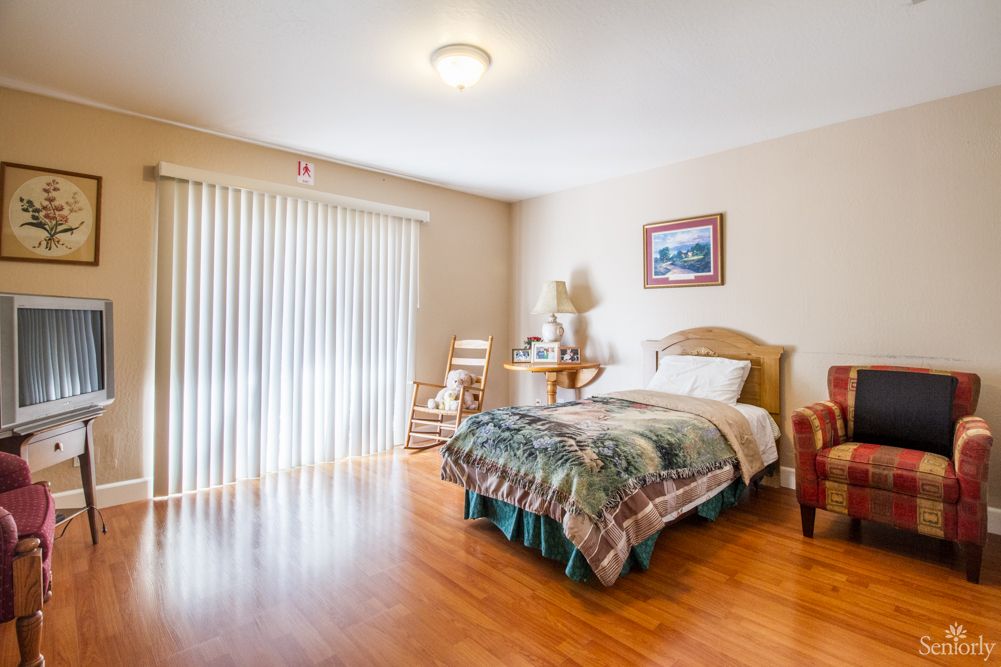 A cozy bedroom with a single bed and wooden flooring, featuring ample natural light from a sliding glass door.