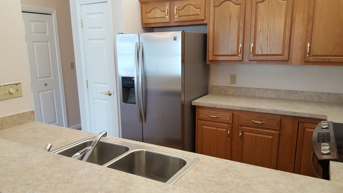 A modern kitchen with a stainless steel refrigerator, dual sink, and wooden cabinets.