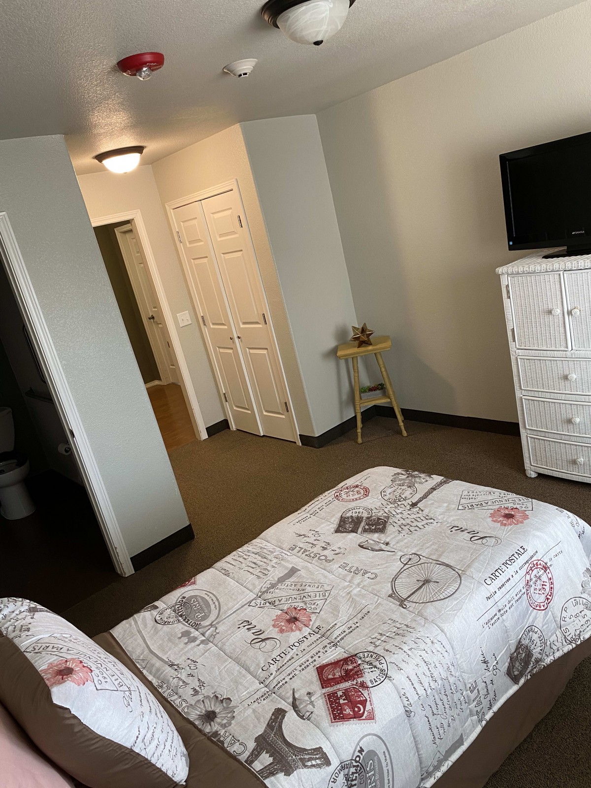 A cozy bedroom with a neatly made bed, dresser, and television.