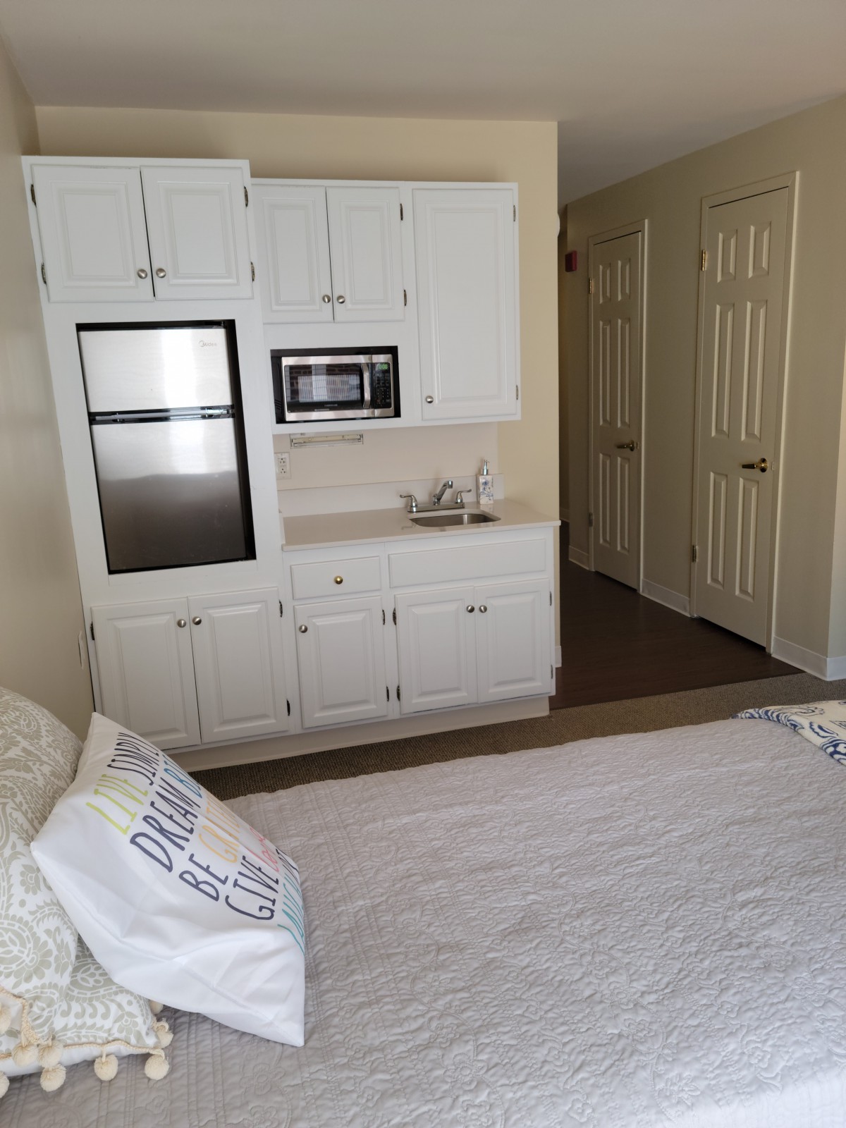 A cozy bedroom featuring built-in white cabinets with a microwave and a comfortable bed.
