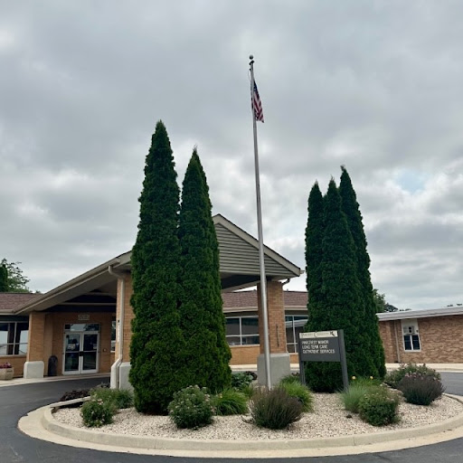 A welcoming entrance with manicured trees and an American flag under a cloudy sky.