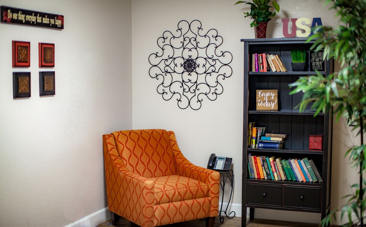 A cozy reading nook with an orange patterned chair, a decorative bookshelf filled with books, and intricate wall art.