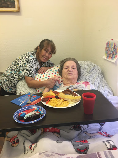 A caregiver provides companionship and a meal to an elderly person in a hospital setting.