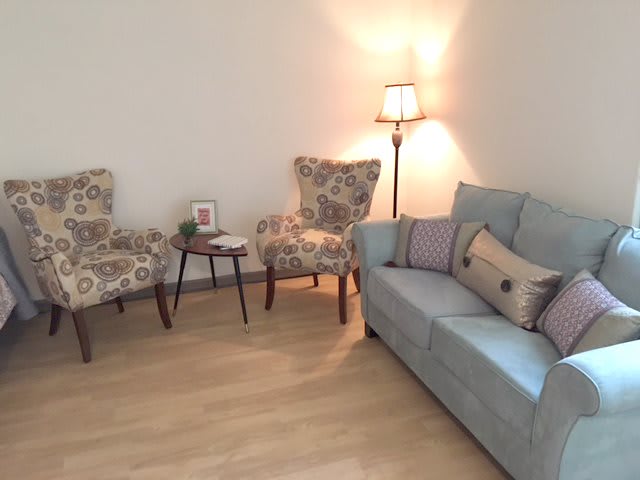A cozy living room setup featuring a sofa, two patterned chairs, a small table, and a floor lamp.