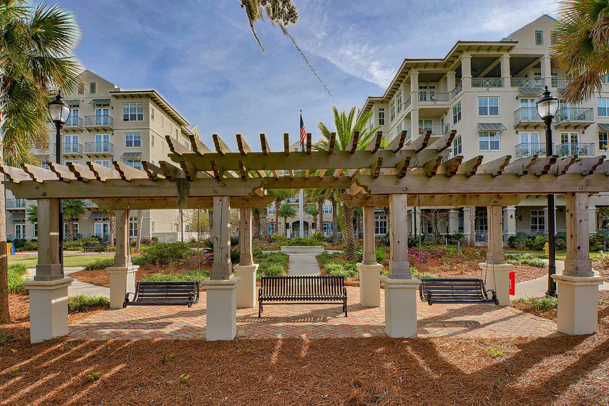 A view of an outdoor area featuring a pergola and benches in front of an apartment complex.