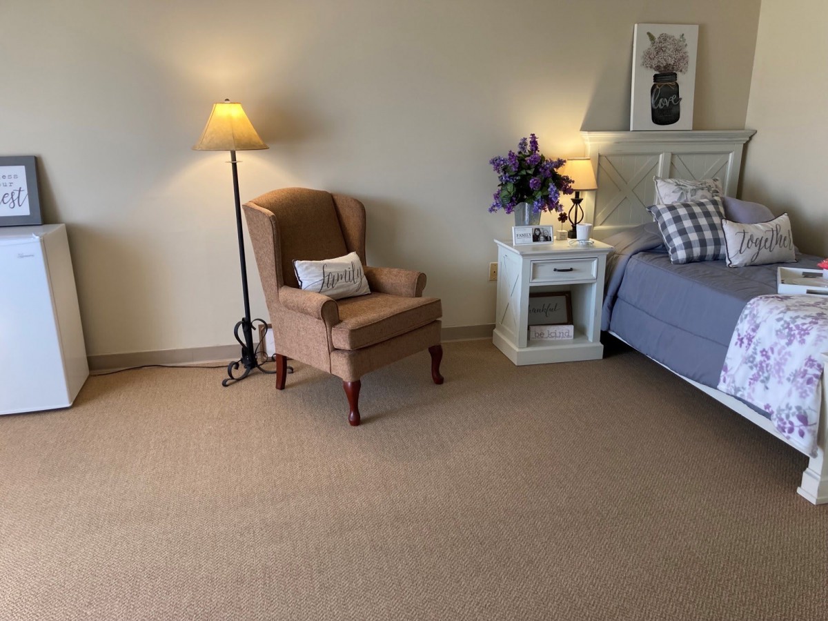 A cozy bedroom with a bed, armchair, and nightstand decorated with flowers.