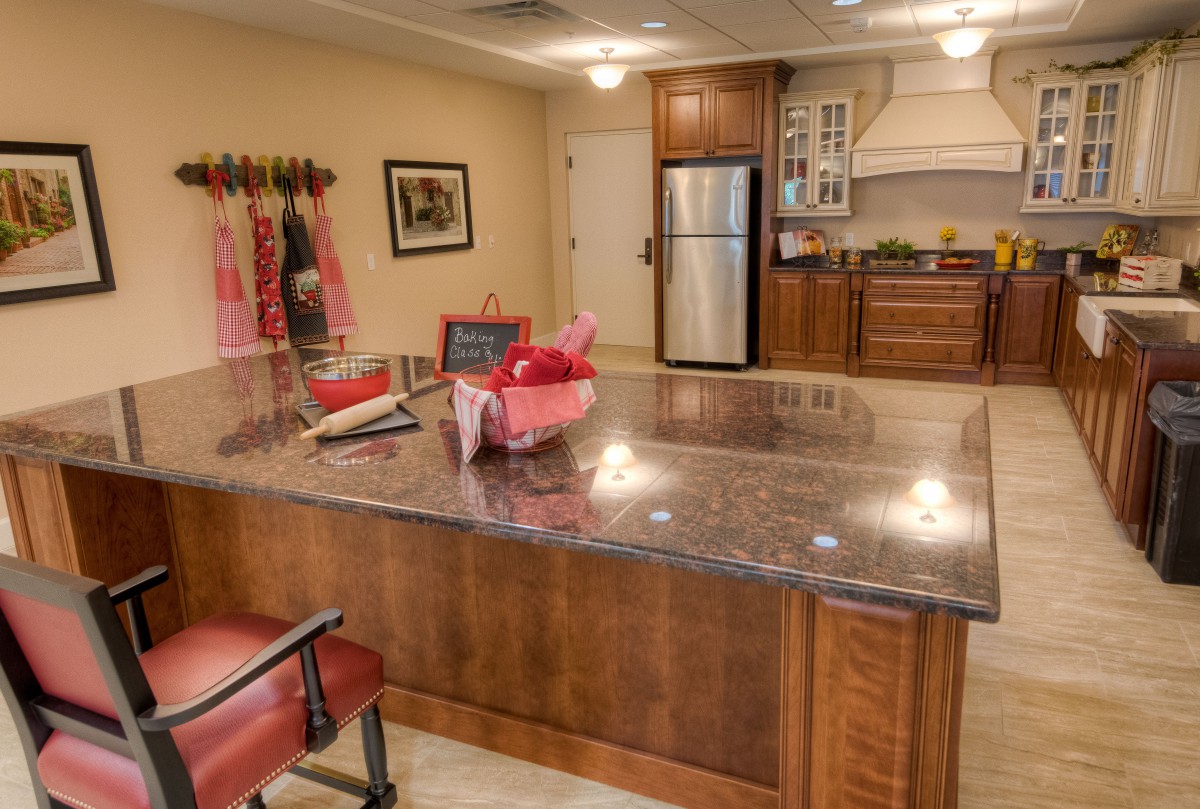 A modern kitchen with a large island counter and stools, featuring wooden cabinets and a stainless steel refrigerator.
